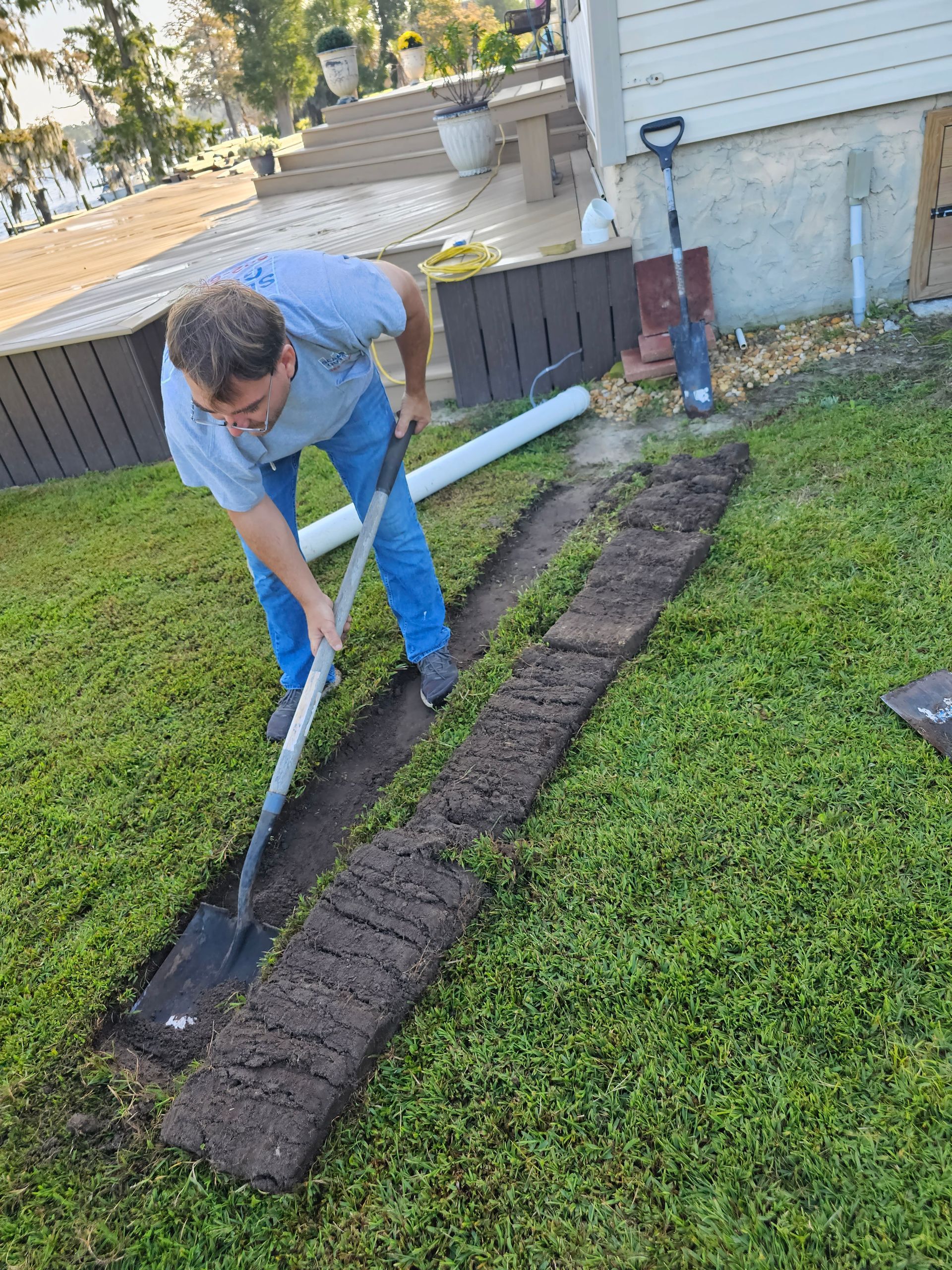 Man digging a trench in a grassy yard, preparing for drainage pipe installation.