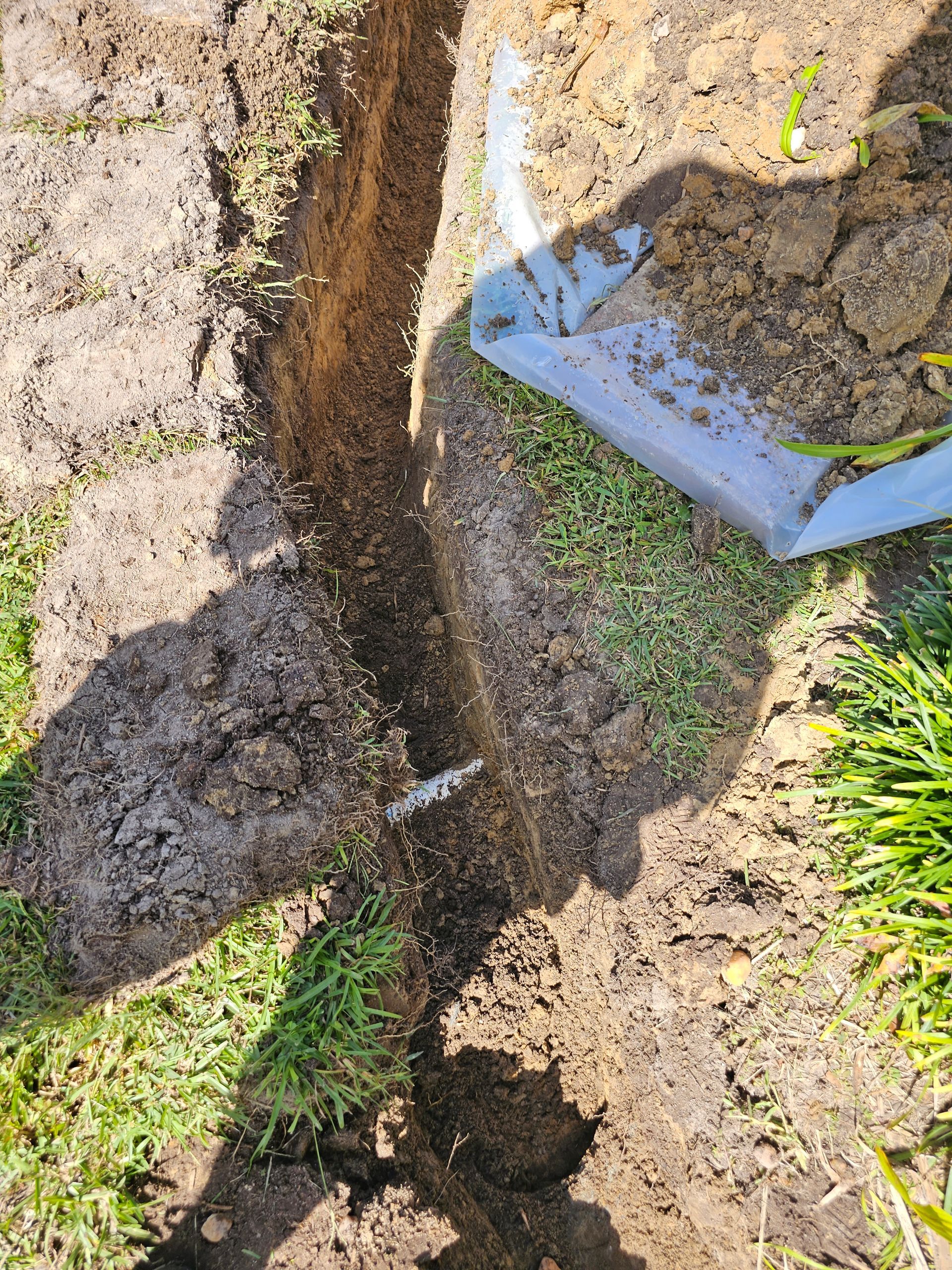 A narrow trench in dirt, white paint on the ground, with a shovel resting nearby.