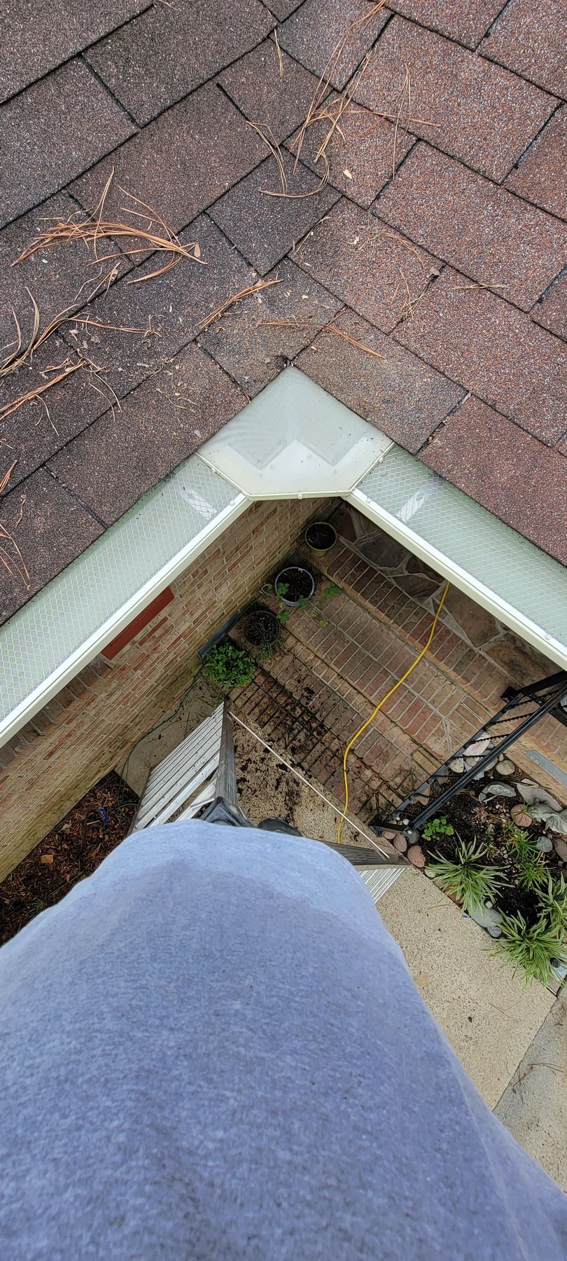 Looking down at a roof corner with a white trim and a person's leg in the foreground.