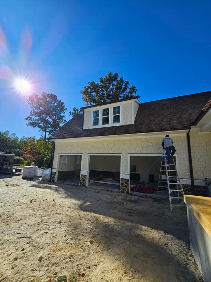 Construction of a house. A person on a ladder works on the garage area under a clear, sunny sky.