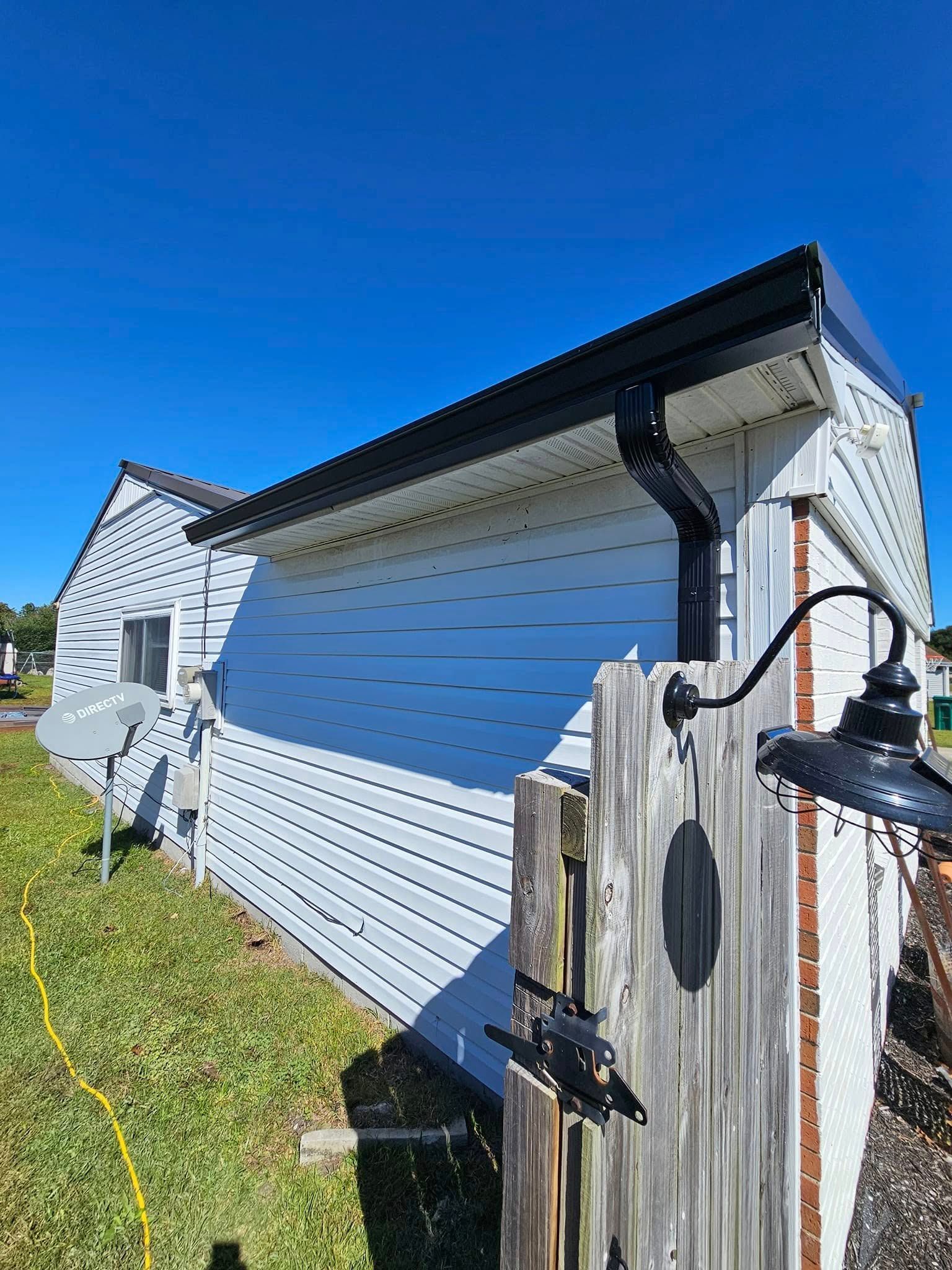 Side view of a white house with black gutters, blue sky, and weathered wooden fence with a black light fixture.