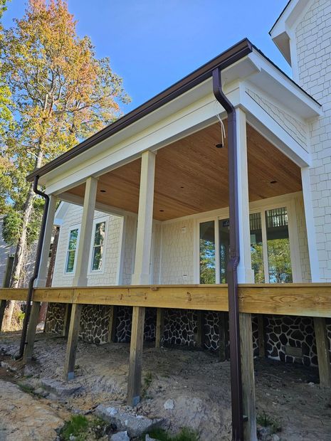 A wooden deck with pillars and a brown roof. House exterior, blue sky, and trees.