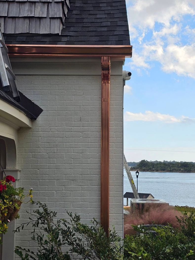 Copper gutters and downspout on a brick house overlooking a waterway on a sunny day.