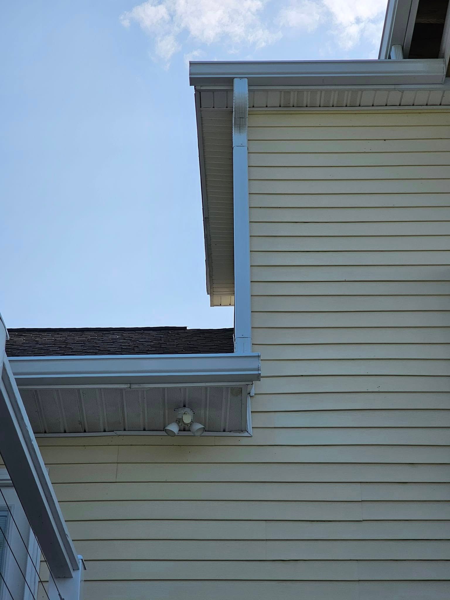 Side of a house with light yellow siding and a white gutter under a blue sky.