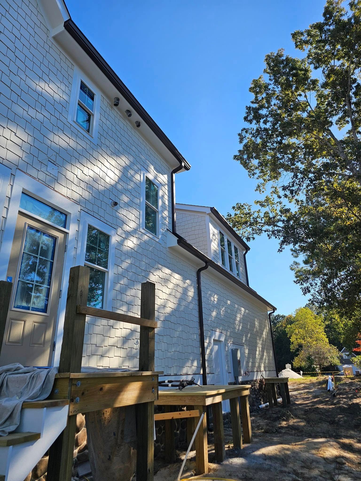 Side view of a house with white siding, dark roof and trim, blue sky, and a partially built wooden deck.