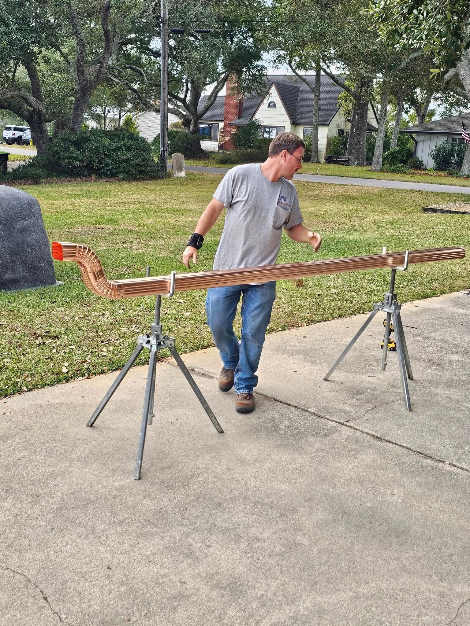 Man inspecting a large wooden snake sculpture supported by tripods on a concrete driveway.