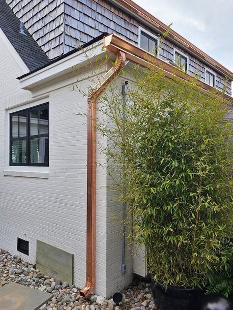 White brick building with copper gutters, black window, and green bushes.