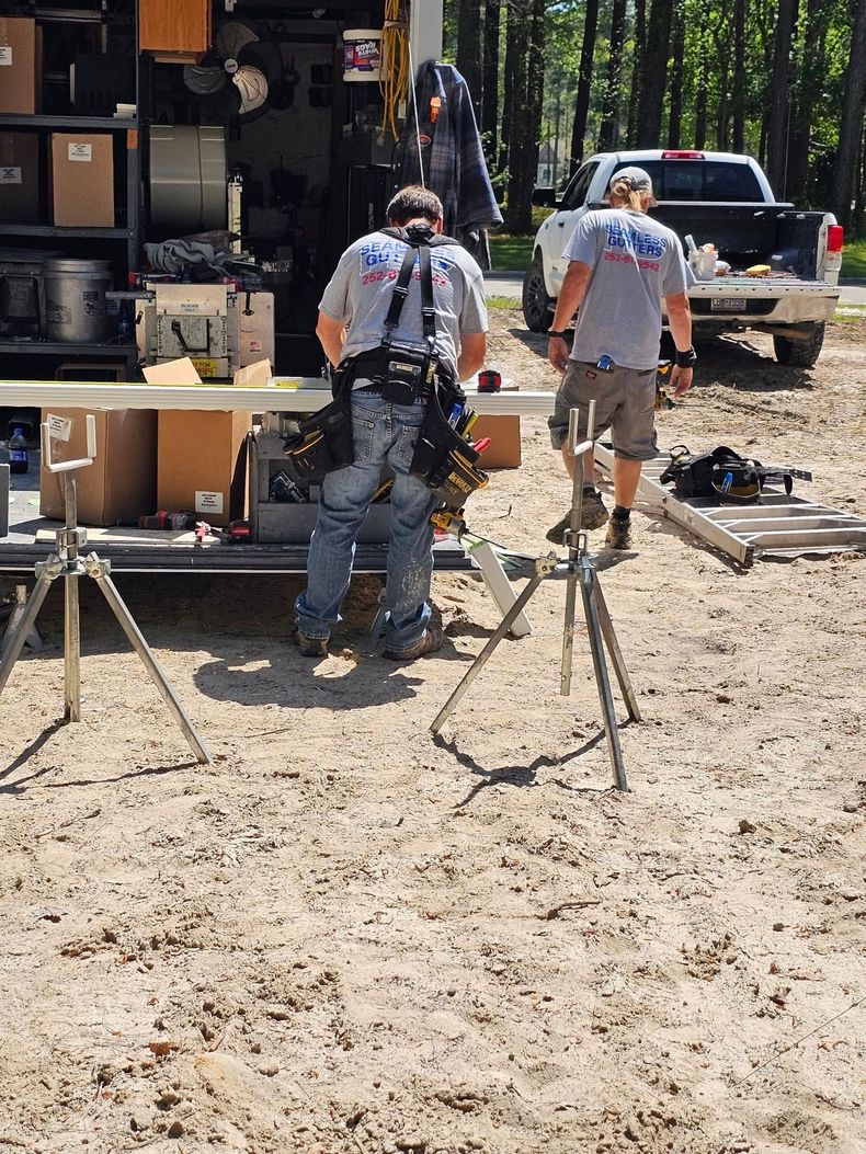 Two construction workers cutting wood outdoors near a truck and tools.