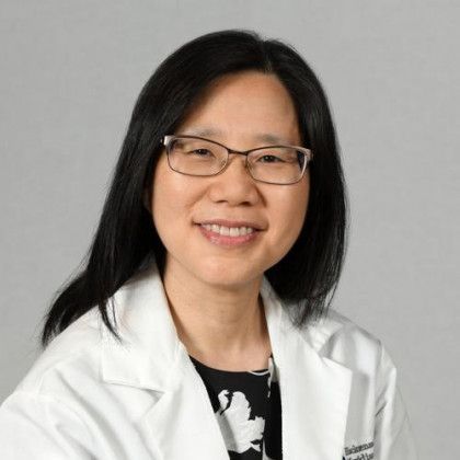 Woman in glasses and white lab coat smiles.