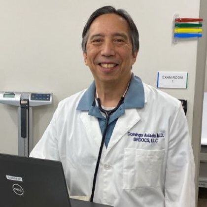 Doctor in a lab coat, stethoscope, smiling, in an exam room.