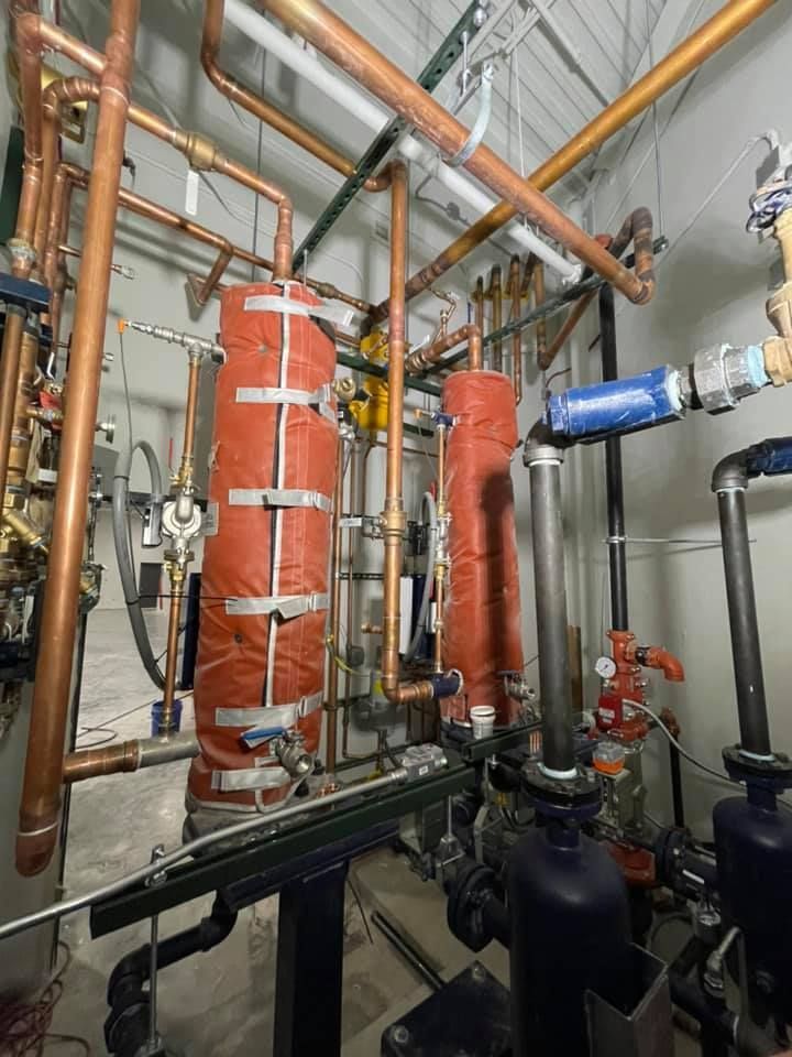 Industrial mechanical room with red insulated pipes, black valves, and copper piping overhead Industrial mechanical room with red insulated pipes, black valves, and copper piping overhead