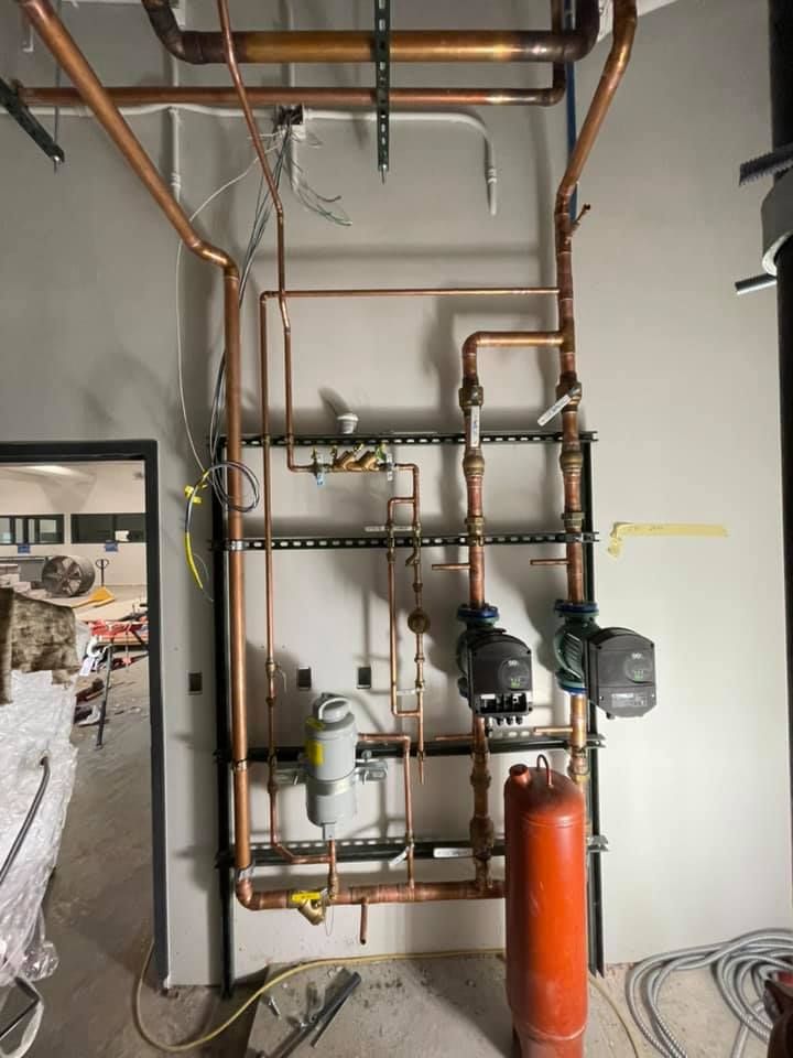 Copper plumbing and valves on a wall, with a red tank in an unfinished utility room. Copper plumbing and valves on a wall, with a red tank in an unfinished utility room.