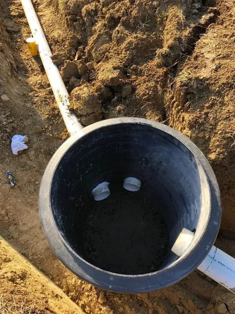 Black utility pipe opening in a dirt trench with white PVC pipes entering from the sides. Black utility pipe opening in a dirt trench with white PVC pipes entering from the sides.