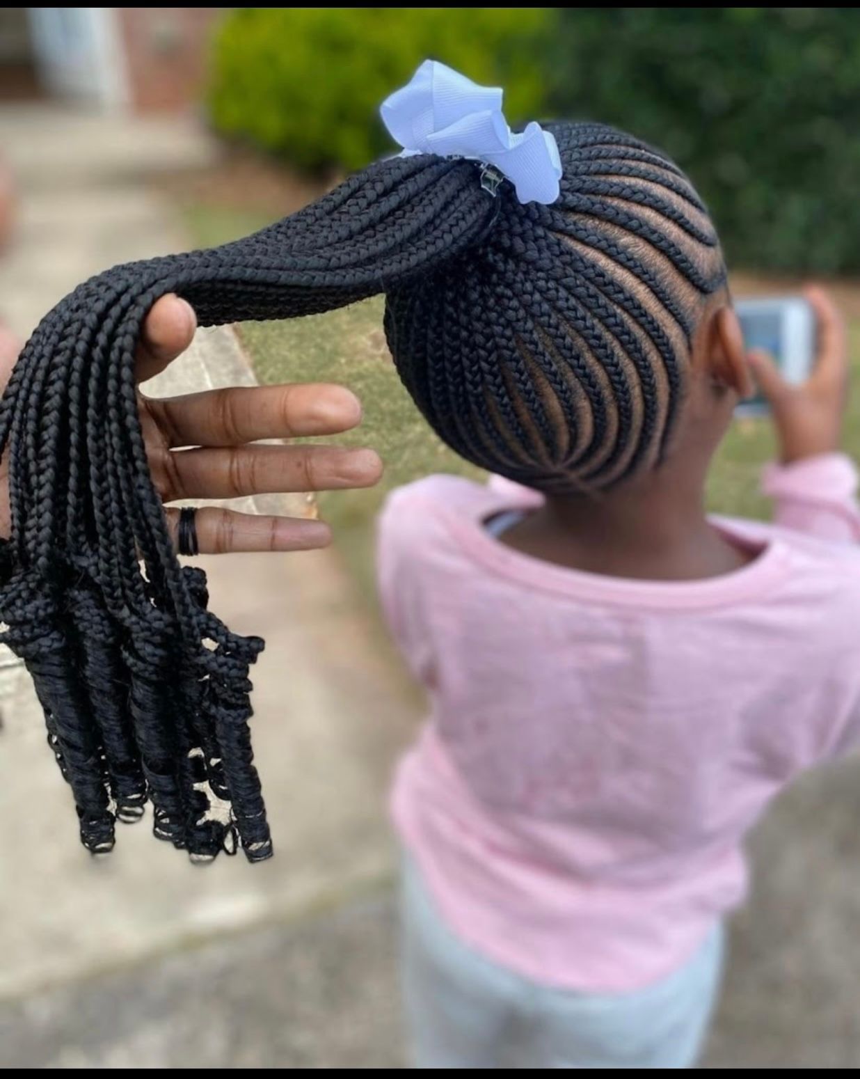 Hands braiding hair with pink ribbon accents on a blonde head