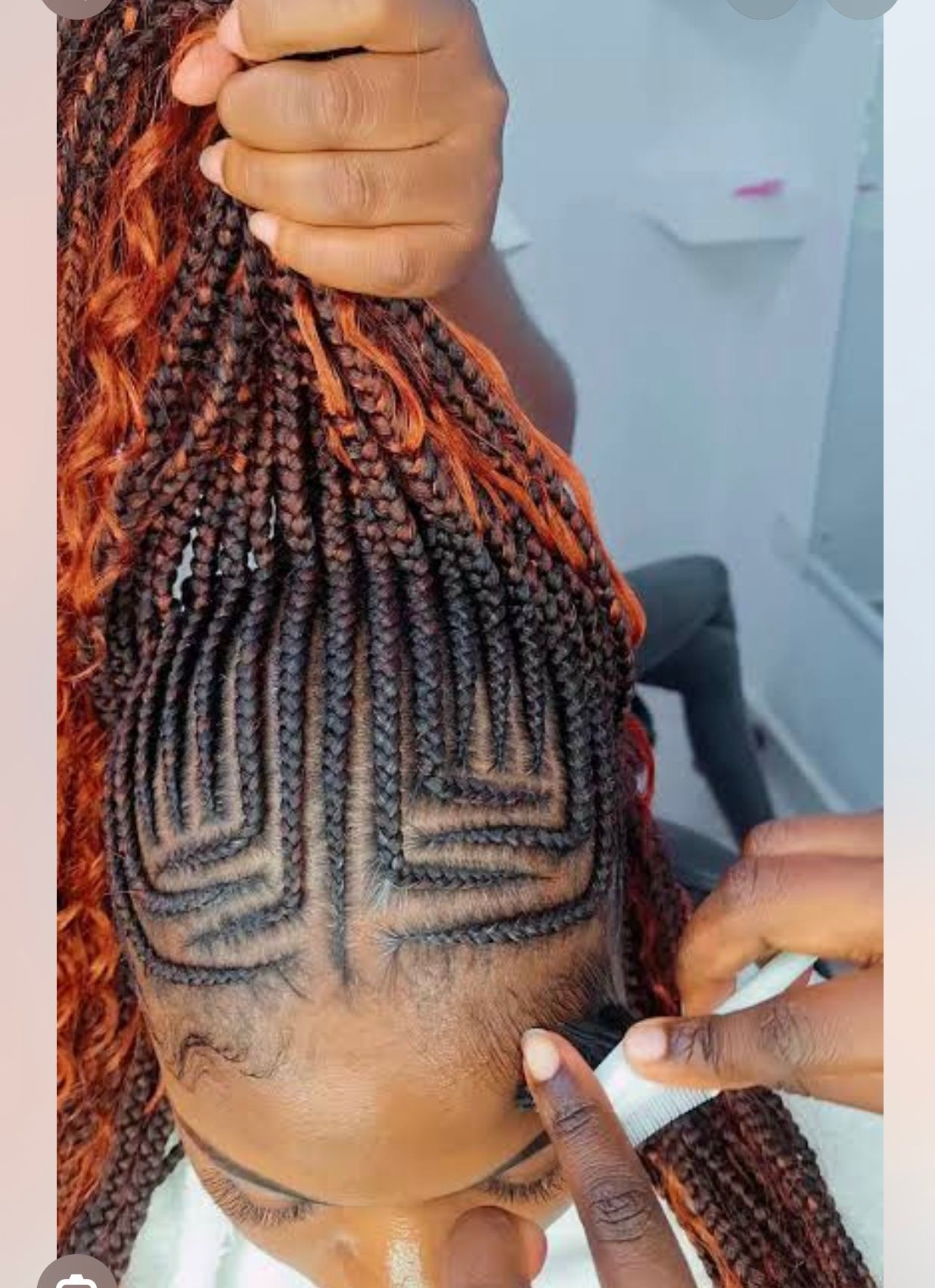 Hands braid colorful pink, orange, and purple hair strands on a child’s head.