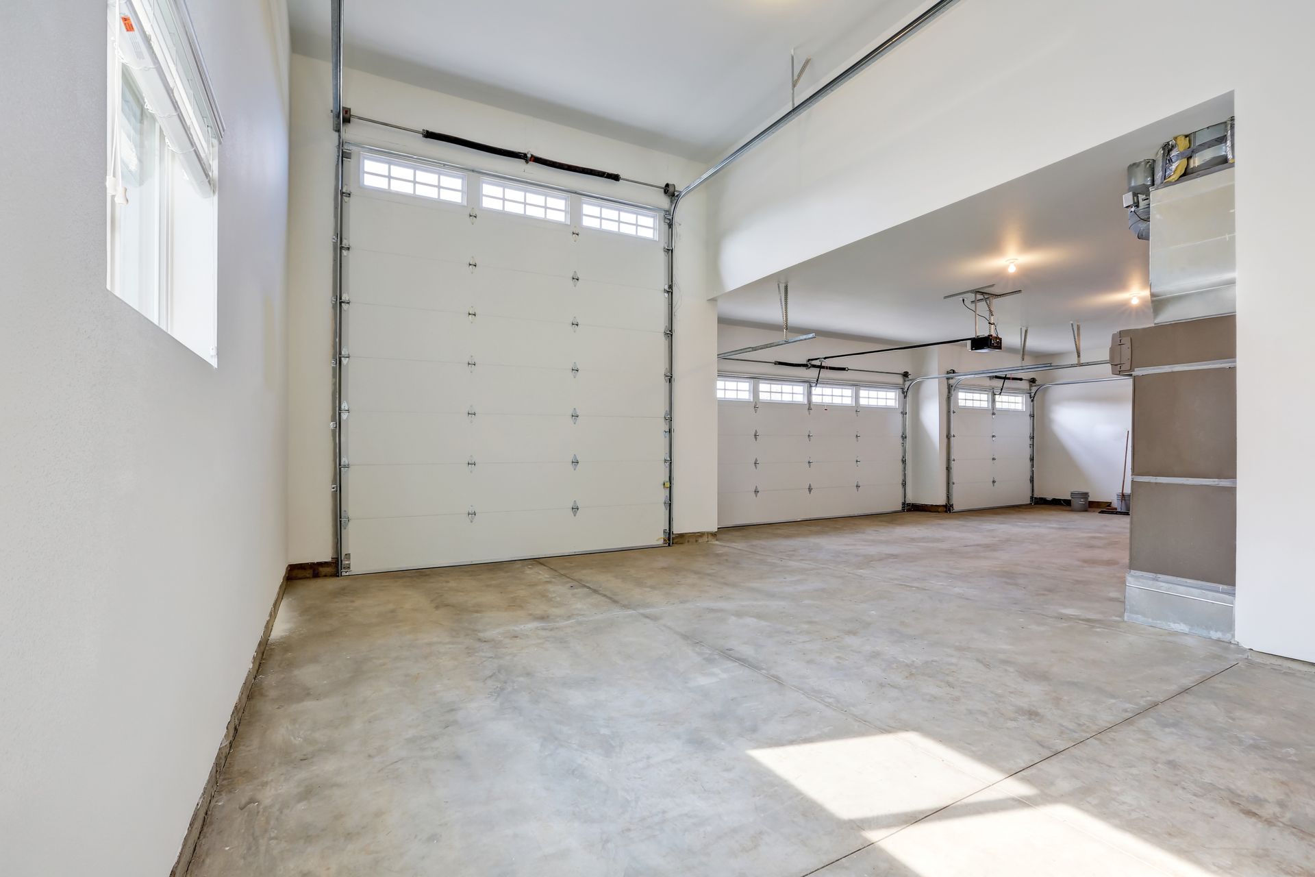 Empty white garage interior with two large overhead doors and a concrete floor