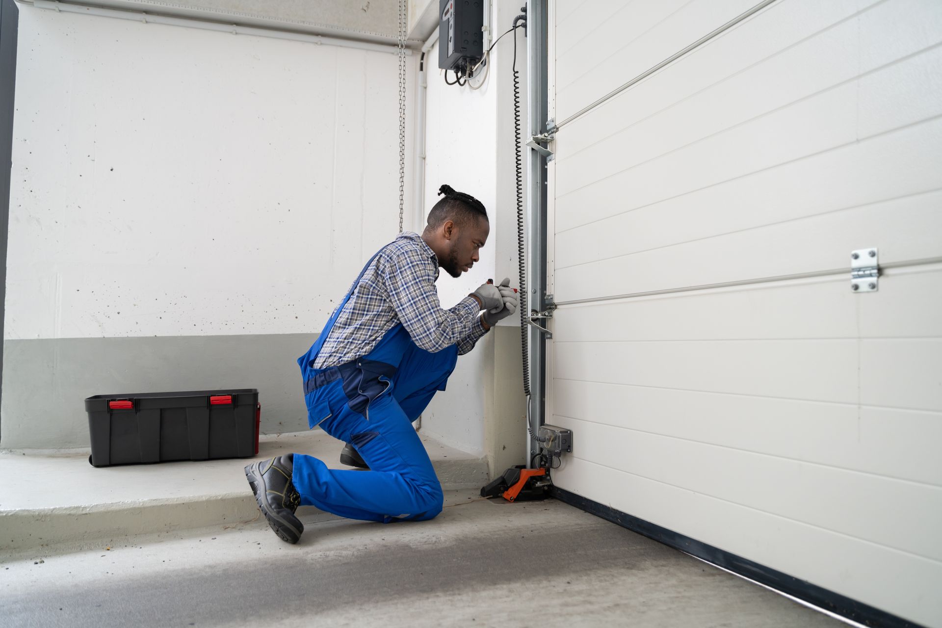 Mechanic kneeling beside a garage door, adjusting the track with a tool.
