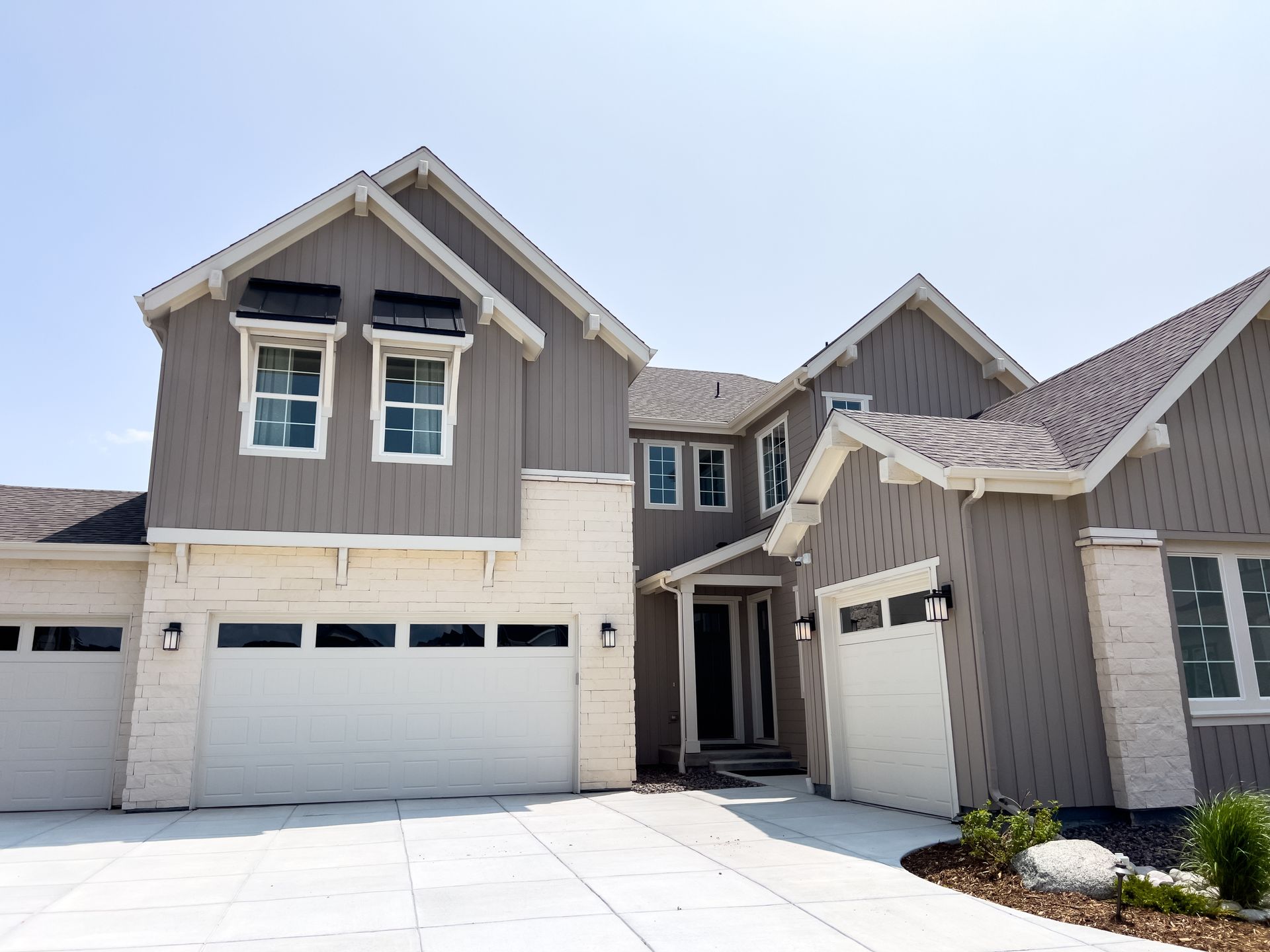 Modern two-story townhouse exterior with beige siding, white garage doors, and snow-covered driveway