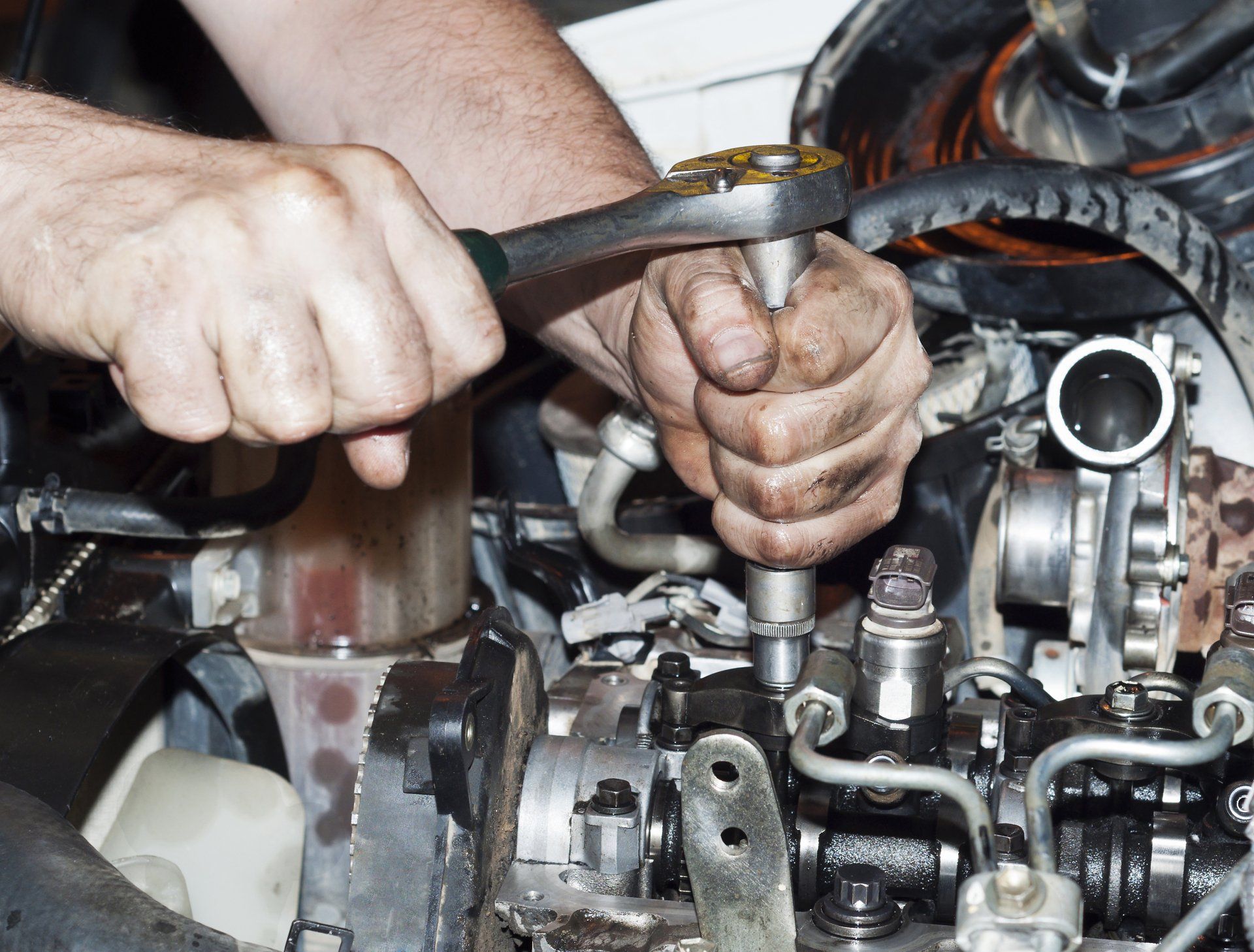 Hands using a wrench to work on a car engine.
