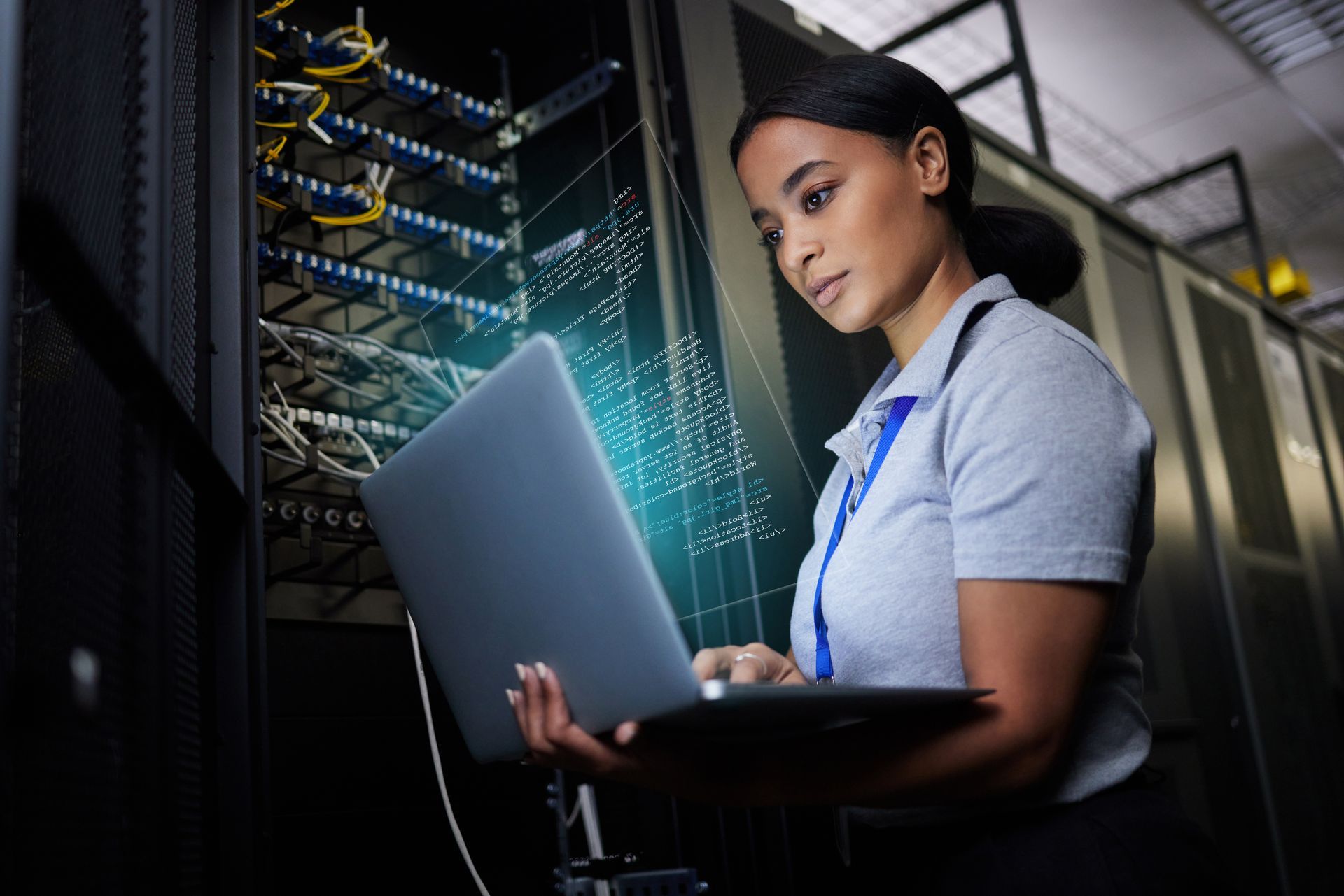 A woman holding a laptop working in a dark server room.