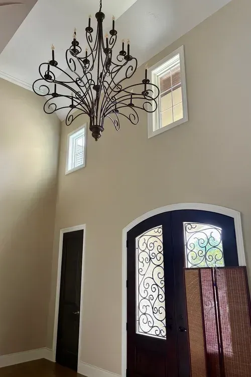 Entryway with chandelier, arched door, dark door, two windows, and beige walls.