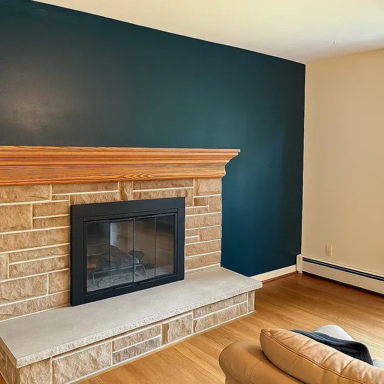 Fireplace with stone facade, dark blue wall, and wooden mantel in a room with hardwood floors.