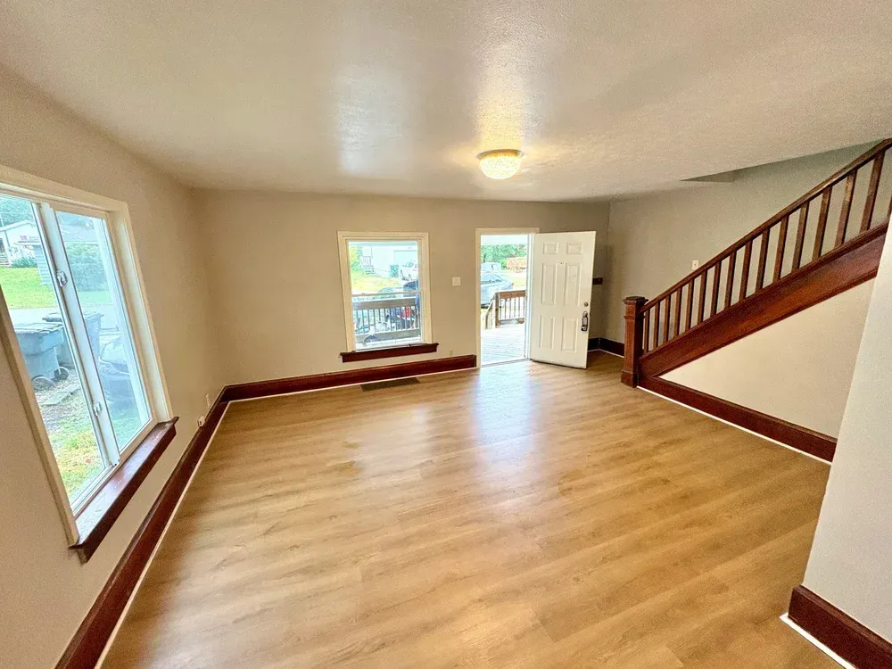 Interior view of a room with wood-look flooring, staircase, windows, and an open doorway leading to a deck.