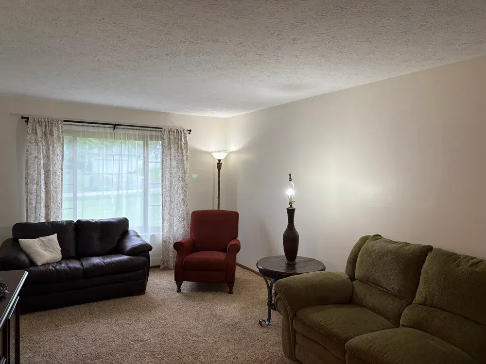 Living room with a brown couch, red chair, green sofa, and a table with a lamp.