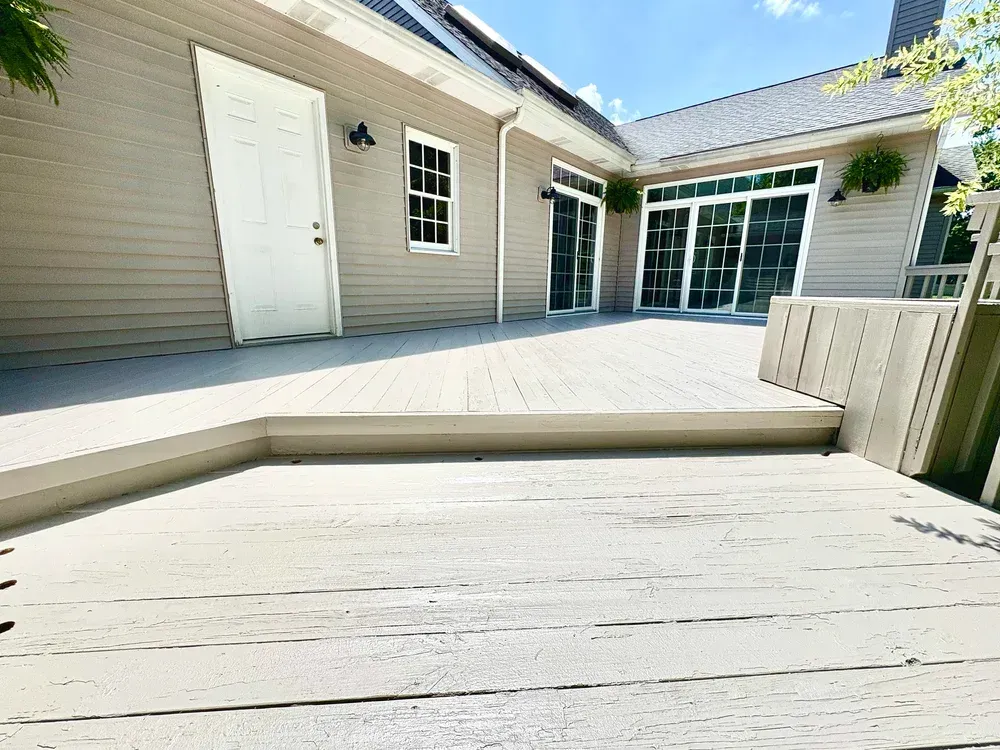 A light-colored wooden deck with steps leading to a house with white door and large glass doors.