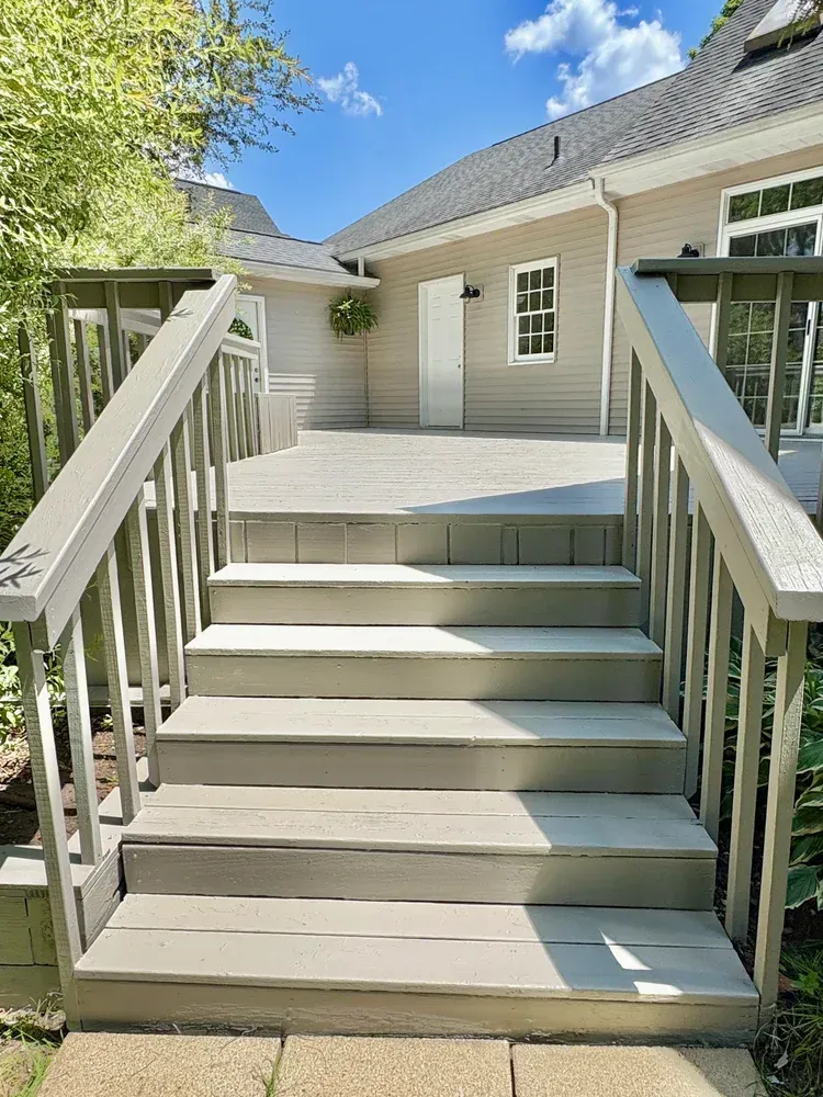Wooden steps leading up to a deck and a light-colored house under a partly cloudy sky.