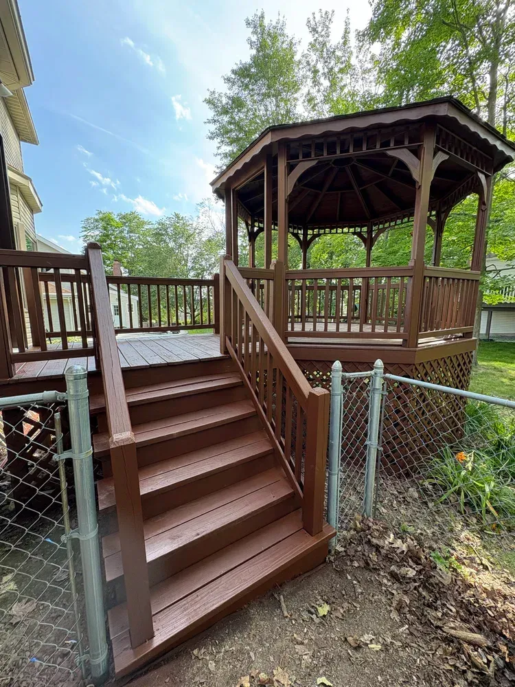 Wooden deck with stairs leading to a gazebo, all painted brown. A chain-link fence borders the yard.