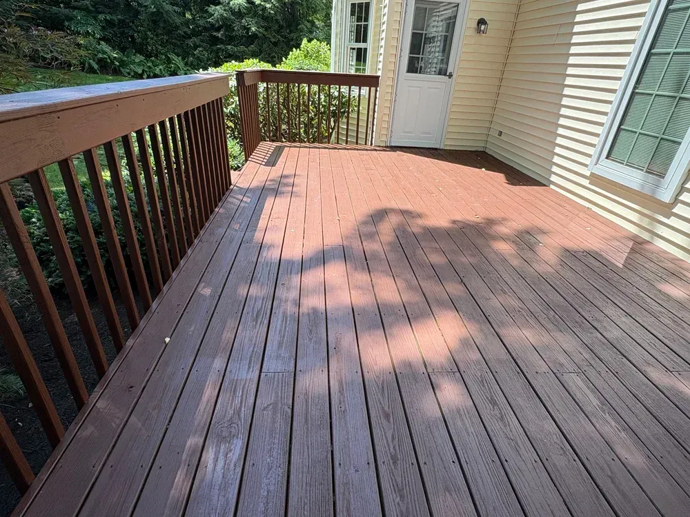Wooden deck with brown stain, railing, and a door, attached to a light-colored house.