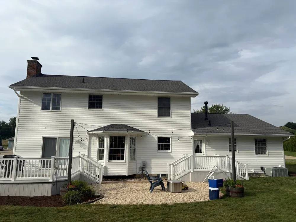 White two-story house with a backyard patio and a deck, under an overcast sky.