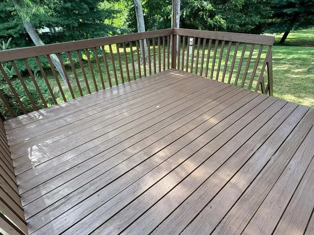 Brown wooden deck with railings, surrounded by green trees.