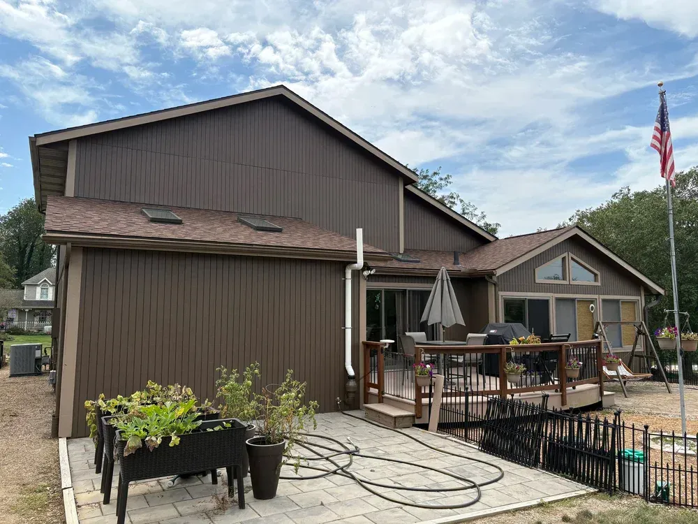 Brown house with a deck and American flag. Planter boxes sit on a patio.
