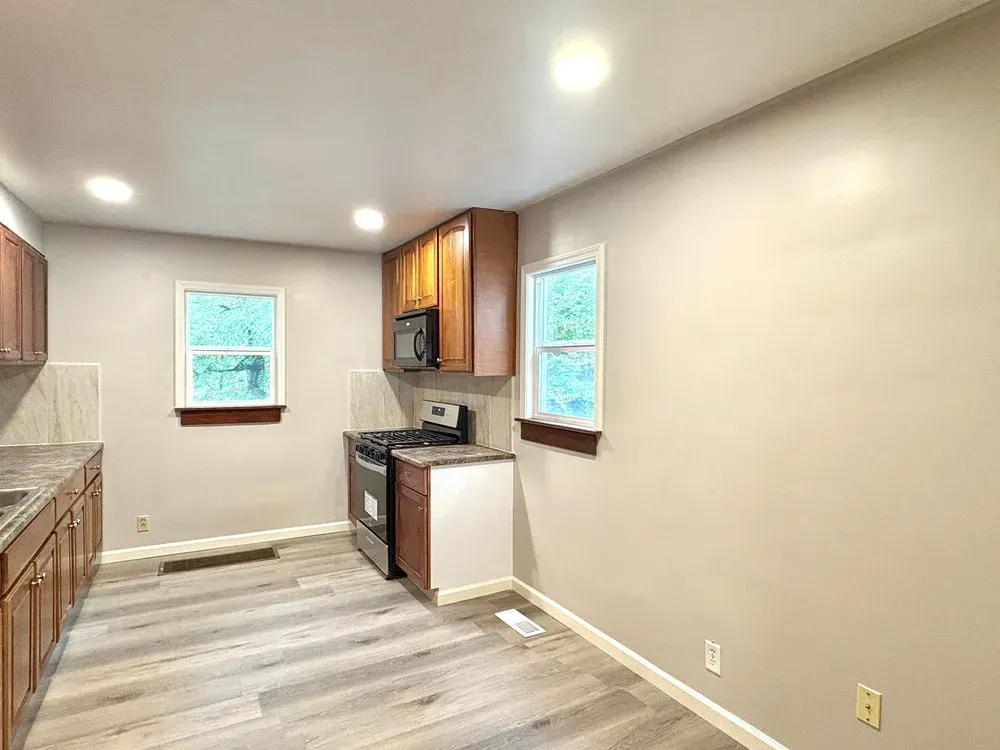 Kitchen with brown cabinets, gray flooring, and two windows.