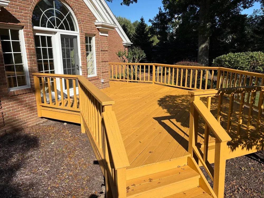 Yellow painted wooden deck with stairs and railings outside a brick house.