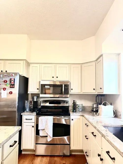 White kitchen with stainless steel appliances, white cabinets, and dark hardware.