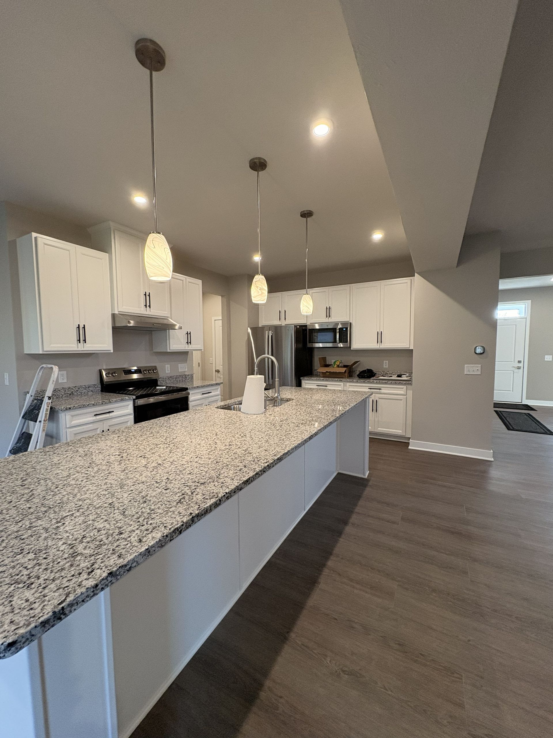 Modern kitchen with white cabinets, granite island, pendant lights, and stainless steel appliances.