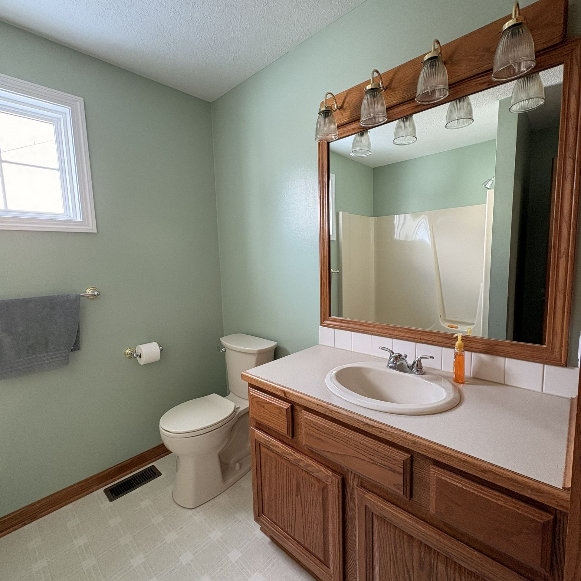 Bathroom with green walls, a white sink and toilet, and a large mirror with a wooden frame.