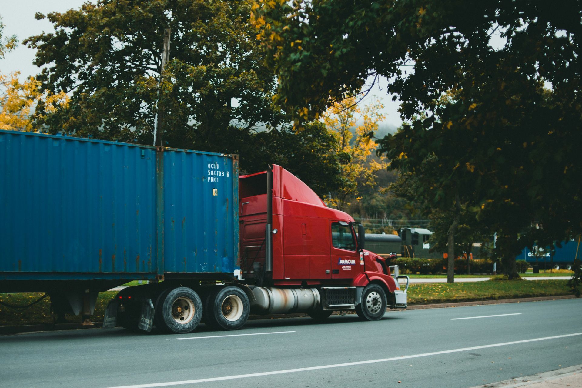 A red semi truck with a blue container on the back is driving down the road.