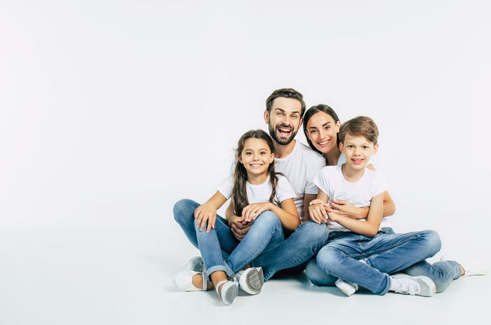 Beautiful and happy smiling young family in white T-shirts are hugging and have a fun time together while sitting on the floor