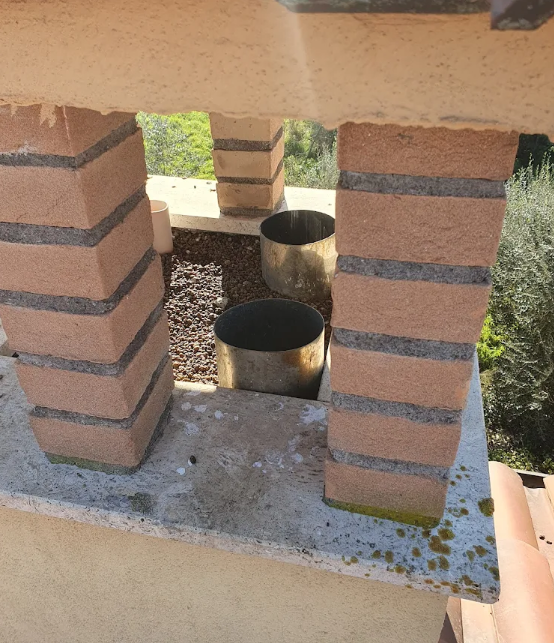 Cima del camino con pilastri in mattoni, canne fumarie metalliche e detriti. Scenario esterno, di giorno.