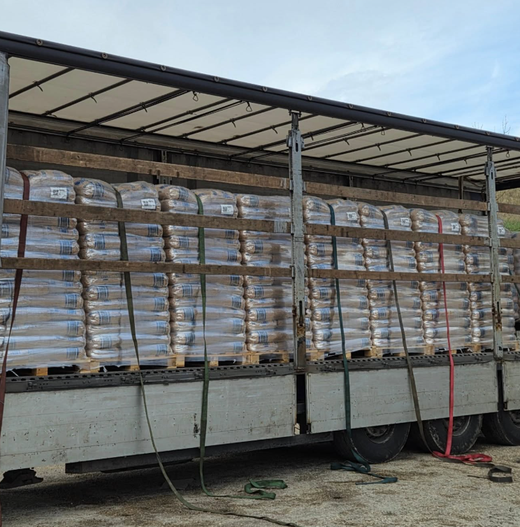 Cassone di camion carico di pallet di sacchi avvolti, fissati con cinghie.