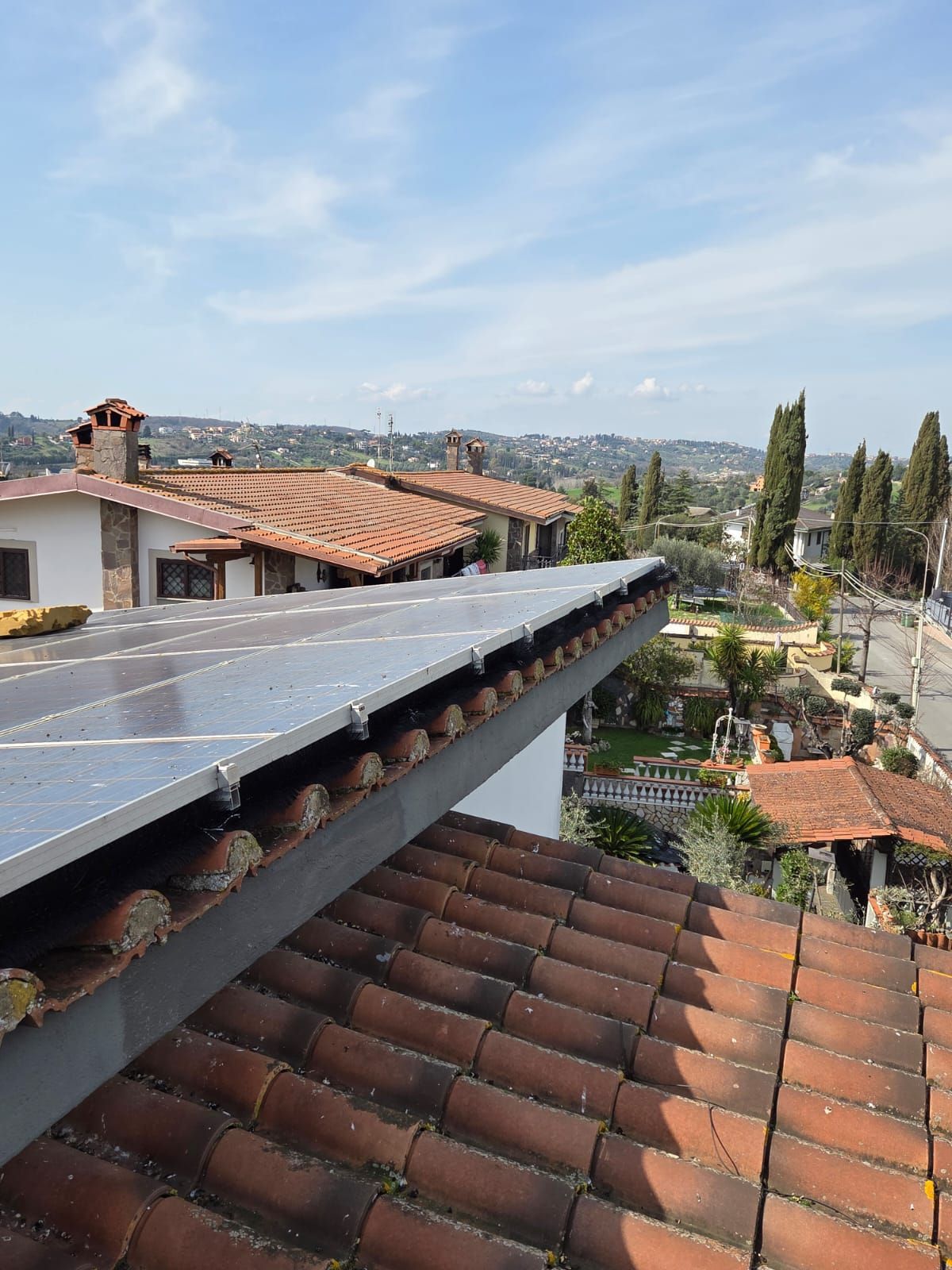 Pannelli solari su un tetto di tegole in terracotta che si affaccia su una zona residenziale con cielo terso.
