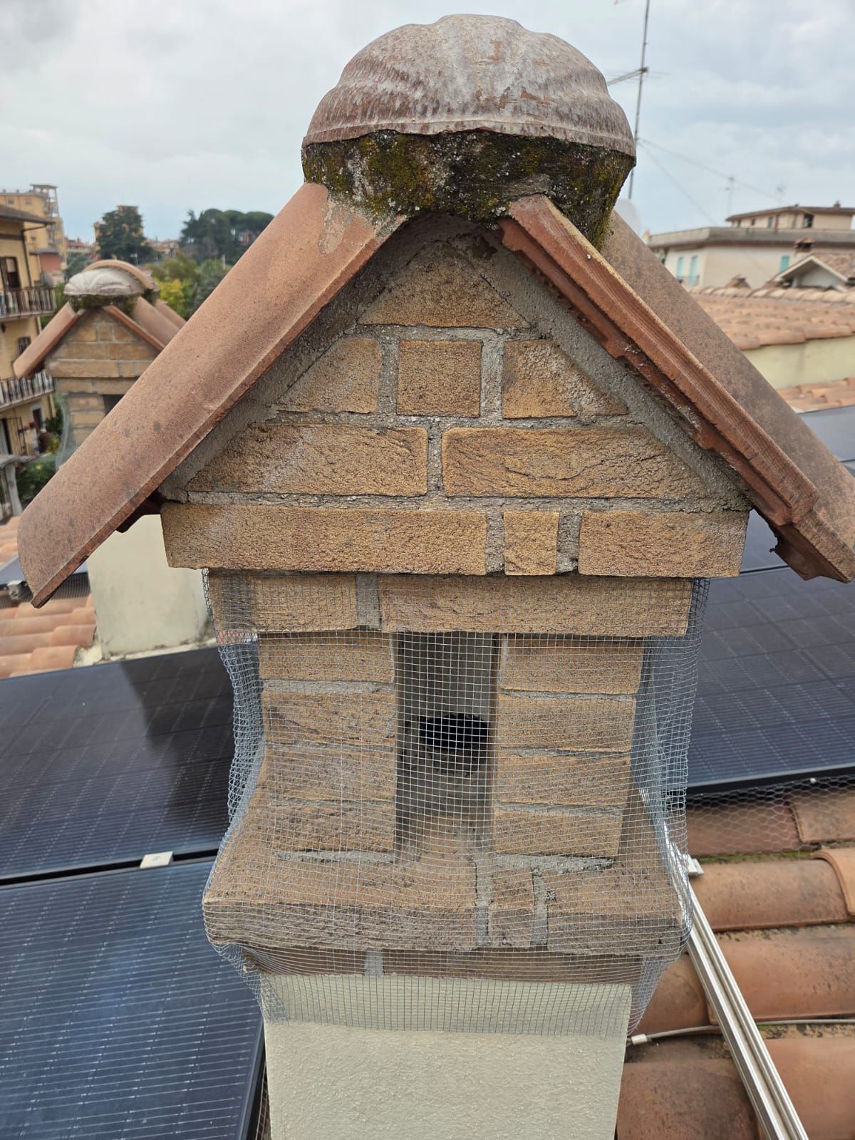 Camino in mattoni con tegole in terracotta e parte superiore decorativa, sullo sfondo di un paesaggio urbano.
