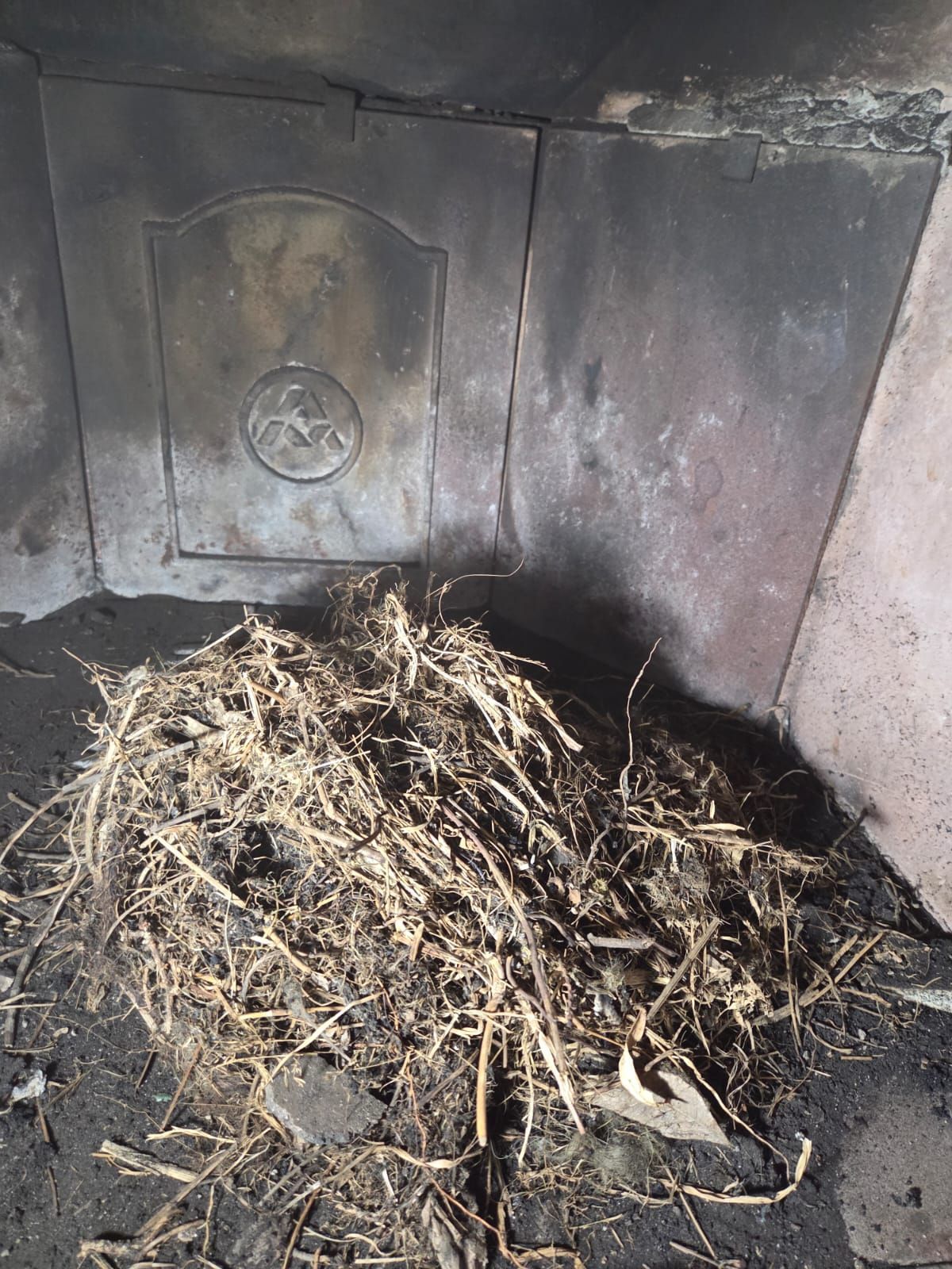Interno del camino con un mucchio di paglia sul pavimento, pareti e porta ricoperte di fuliggine.