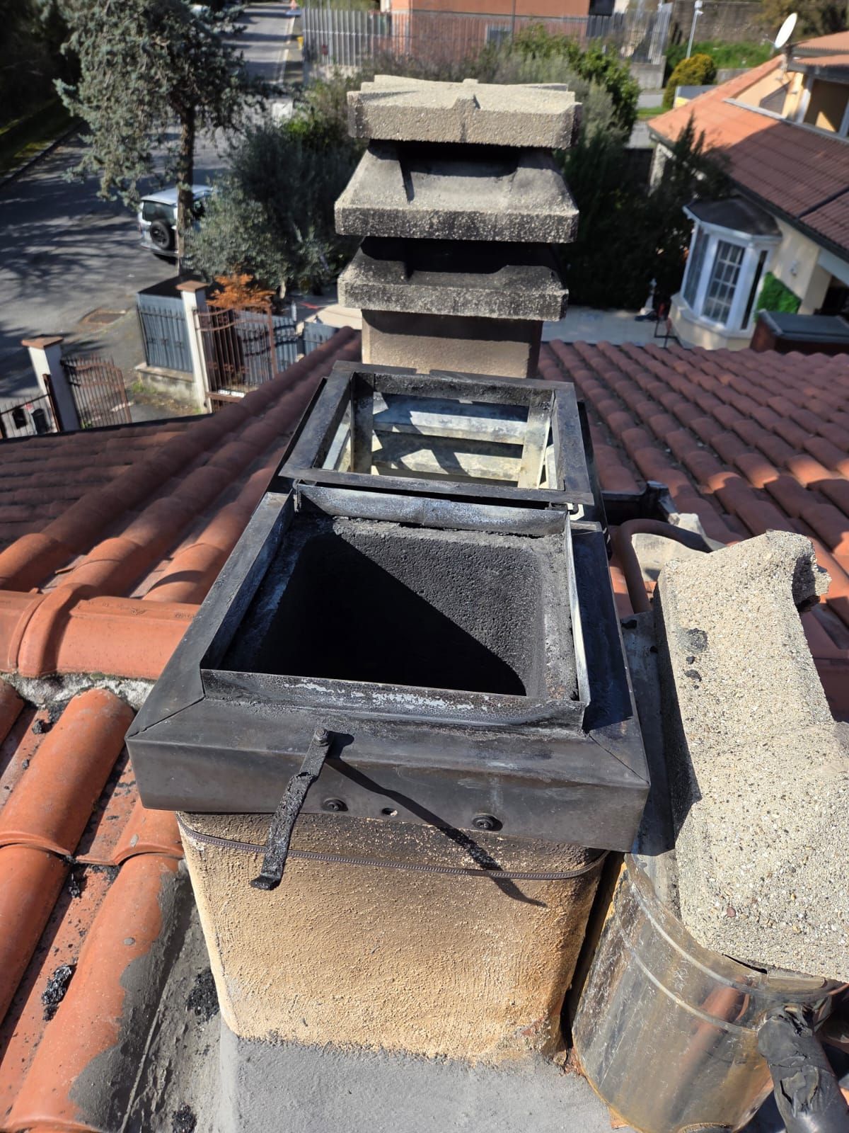 Camino su un tetto di tegole rosse, aperto con fuliggine visibile e con un cappello a più livelli.