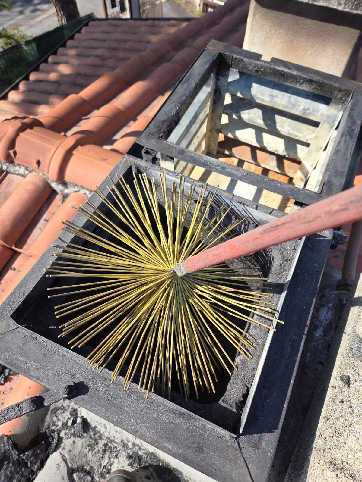 Camino pulito con una spazzola gialla dalla sommità di un tetto con tegole rosse.
