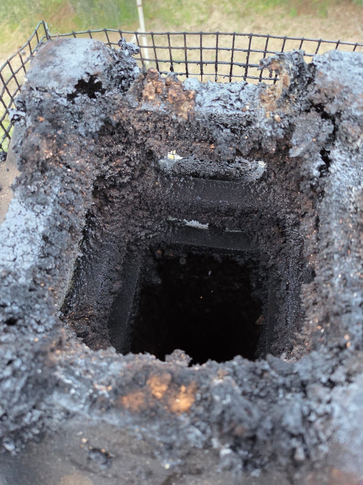 Vista dall'alto di un camino quadrato. La parte interna e superiore sono ricoperte da una patina di fuliggine nera. La parte superiore è coperta da una rete metallica.
